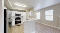 This single-floor residence is designed with a clean, contemporary aesthetic characterized by neutral warm-beige tones, light wood-style flooring, and an abundance of natural light throughout. The open-concept layout connects the kitchen and living area seamlessly, creating a welcoming, airy atmosphere.

The kitchen is well-equipped with stainless steel appliances, including a gas range, microwave, and refrigerator, complemented by crisp white cabinetry, a classic subway tile backsplash, and a peninsula with a built-in sink that provides additional counter space and casual dining potential.

The spacious living area features light wood-style flooring, multiple windows that invite generous natural light, and a fireplace with a built-in display niche above, serving as a functional focal point. An additional room with large windows and light flooring offers flexibility as a dining or office space.

The bedrooms are carpeted for comfort and include ample natural light from well-positioned windows. A generous walk-in closet with wire shelving systems provides organized storage. The bathrooms are finished with white vanities, light countertops, and chrome fixtures; one features a tub-shower combo, while the other offers a separate vanity area adjacent to a tub-shower.