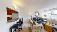 Located at 700 W Browning Rd in Collingswood, NJ, this single-floor residence offers a thoughtfully designed layout that balances comfort and functionality. The living room serves as the centerpiece of the home, featuring large windows with vertical blinds that allow generous natural light to fill the carpeted space. A decorative sunburst mirror, ladder-style bookshelf, and a combination of a tufted leather sofa and patterned accent chairs contribute to an inviting, stylish atmosphere. A breakfast bar with seating connects the living area to the kitchen, creating an open, social flow. The kitchen is well-equipped with warm wood cabinetry, dark granite-style countertops, a gas range, dishwasher, microwave, and refrigerator, offering ample storage and prep space. The bedroom is a serene retreat, complete with plush carpeting, a ceiling fan, and a wide window that brings in natural light and outdoor views. A built-in closet provides practical storage. The bathroom features classic tile wall accents in warm tones, a vanity with under-sink storage, and a shower-tub combination. Throughout the residence, neutral walls and soft flooring create a cohesive, comfortable ambiance suitable for everyday living.