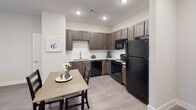 Located at 1561 Red Bud Ln in Round Rock, Texas, this single-story unit offers a thoughtfully designed open-concept floor plan that seamlessly connects the kitchen, dining area, and living room. Light-toned wood-style flooring runs throughout, contributing to a cohesive and clean aesthetic across the space.

The kitchen is well-equipped with dark espresso cabinetry, light countertops, a white subway tile backsplash, and black appliances including a refrigerator, range, microwave, and dishwasher. A pantry closet provides additional storage nearby. The dining area sits adjacent to the kitchen, offering a natural transition into the living room, which features recessed lighting, a ceiling fan, and access to a patio through glass doors that bring in natural light.

The bedroom is generously proportioned with a ceiling fan, large windows, and a walk-in closet with built-in shelving. The neutral gray walls and wood-style flooring continue throughout, maintaining a calm and consistent atmosphere. The bathroom features a dark vanity with a granite-style countertop, a mirror with overhead lighting, and wood-style tile flooring. Overall, the space presents a modern, functional design with clean finishes throughout.
