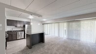 Located at 6310 Greenspring Ave in Baltimore, MD, this two-bedroom, one-bathroom residence offers a well-designed single-floor layout. The open-concept living and kitchen area forms the heart of the home, where a dark-cabinetted kitchen with stainless steel appliances — including a refrigerator, range with hood vent, and dishwasher — pairs with granite countertops and a subway tile backsplash. Light wood-look flooring runs throughout the kitchen, while a central island with a granite top provides additional prep and dining space with pendant lighting above. The adjoining living room is expansive and carpeted, with floor-to-ceiling vertical blinds spanning a wide wall of windows and a sliding glass door, allowing abundant natural light and access to an outdoor balcony with green wooded views. The generously sized primary bedroom offers large windows framing lush tree views and plush carpet flooring. The second bedroom is similarly carpeted and well-lit with natural light. An in-unit washer and dryer is conveniently included. Throughout the residence, a neutral color palette and clean lines create a calm, functional ambiance suited for comfortable everyday living.