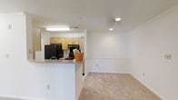 This single-floor, 1-bedroom, 1-bathroom unit offers a practical and comfortable living space designed for everyday ease. The open-concept layout connects the kitchen and living area seamlessly, creating a sense of spaciousness. The kitchen is outfitted with light wood cabinetry, black appliances including a refrigerator and range, and a peninsula counter that doubles as a casual dining or prep area. A flush-mount light fixture brightens the kitchen workspace, while recessed lighting in the adjoining living area adds a clean, modern touch. The living area features neutral-toned carpet, providing a warm and inviting atmosphere. The walls are painted in a crisp, neutral white that enhances the brightness of the space and complements the overall design. The layout flows naturally, making the unit feel open while maintaining a cozy residential character. The consistent finishes throughout the main living and kitchen areas contribute to a cohesive and move-in-ready aesthetic, well-suited for individuals or couples seeking a comfortable, efficiently designed home.