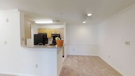 This single-floor, 1-bedroom, 1-bathroom unit offers a practical and comfortable living space designed for everyday ease. The open-concept layout connects the kitchen and living area seamlessly, creating a sense of spaciousness. The kitchen is outfitted with light wood cabinetry, black appliances including a refrigerator and range, and a peninsula counter that doubles as a casual dining or prep area. A flush-mount light fixture brightens the kitchen workspace, while recessed lighting in the adjoining living area adds a clean, modern touch. The living area features neutral-toned carpet, providing a warm and inviting atmosphere. The walls are painted in a crisp, neutral white that enhances the brightness of the space and complements the overall design. The layout flows naturally, making the unit feel open while maintaining a cozy residential character. The consistent finishes throughout the main living and kitchen areas contribute to a cohesive and move-in-ready aesthetic, well-suited for individuals or couples seeking a comfortable, efficiently designed home.
