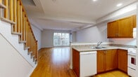 Located at 20 York St in Ottawa's vibrant Lowertown neighbourhood, this two-storey residence offers a well-organized layout spread across two floors. The main floor features an open-concept design where the kitchen flows seamlessly into the living area. The kitchen is outfitted with warm wood cabinetry, granite-style countertops, a peninsula with a sink, and white appliances including a refrigerator, stove, and dishwasher. Hardwood flooring runs throughout the main level, adding warmth and continuity to the space. A staircase with a classic wood banister connects the two floors. Large sliding glass doors on the main level draw in natural light and offer views to the exterior. The upper floor transitions to plush carpeting and includes a generously sized living room with a large sliding door that opens to a balcony, providing additional outdoor access and natural light. A bedroom with double closet doors offers ample storage. The bathroom features a full soaking tub with tiled surround and clean, neutral finishes. The overall aesthetic throughout is clean and neutral, with light walls and practical finishes that create a bright, functional living environment.