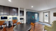 Located at 3405 N Shepherd Dr in Houston, TX, this single-floor community amenity space is thoughtfully designed to serve residents with a variety of practical and social functions. Warm hardwood-style flooring runs throughout, lending a cohesive and inviting feel to the entire area.

The fully equipped kitchen is a standout feature, showcasing rich dark-stained cabinetry extending from floor to ceiling, light granite countertops, a white tile backsplash, stainless steel appliances including a full-size refrigerator, a dishwasher, a microwave, and a sink. Stylish pendant lights hang above a breakfast bar with seating, making it ideal for casual dining or socializing.

The main lounge area offers a round dining table with chairs, creating a comfortable gathering space. A wall-mounted TV and a pair of accent chairs provide a relaxed seating nook near the exterior door, which allows natural light to filter into the space. A built-in business center workstation with cabinetry above offers a dedicated computer setup for resident use.

A prominent Amazon Hub package locker station provides secure and convenient parcel retrieval. An adjacent fitness room, visible through a doorway, features cardio equipment including a treadmill. Recessed lighting throughout ensures the space remains bright and functional at all times.