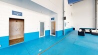 This state-of-the-art aquatic center, located at 1735 Tribe Dr in Biloxi, MS, boasts a spacious 7,110 square foot single-story layout. The facility's centerpiece is a large, pristine swimming pool with clearly marked lanes, ideal for lap swimming and aquatic exercises. The pool area is enveloped by expansive glass walls, allowing ample natural light to flood the space and creating an open, airy atmosphere.

The interior is characterized by a striking blue and white color scheme, with blue-tiled pool walls and a matching blue floor that extends throughout the facility. This cohesive design creates a visually appealing and energizing environment. Safety features are prominent, including multiple ladders for pool access, handrails, and clearly visible emergency equipment.

The building's architecture showcases a modern industrial style with exposed ceiling beams and ductwork. High ceilings contribute to the sense of spaciousness and improve air circulation. Adjacent to the pool area, the facility includes additional rooms, likely for changing areas, equipment storage, or staff offices.

Designed for accessibility, the space features wide doorways and a layout that appears to accommodate individuals with varying mobility needs. The "Move Well" sign visible in one image suggests a focus on health and fitness, indicating that this facility may offer therapeutic or fitness-oriented aquatic programs.