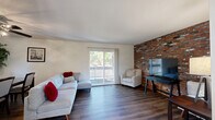 This well-appointed three-story home offers 2 bedrooms and 3 bathrooms across a thoughtfully laid-out floor plan. A defining architectural feature throughout is the striking exposed brick accent wall, which appears in the living room, dining area, and primary bedroom, lending a warm, urban-industrial character to the interiors.

The main living level serves as the social hub of the home, where an open living and dining area is anchored by rich hardwood-style flooring and sliding glass doors that lead to a patio, flooding the space with natural light and outdoor views. The kitchen is outfitted with warm wood cabinetry, granite-style countertops, a tile backsplash, and black appliances, complemented by a window overlooking greenery outside.

Carpeted staircases with wood-trimmed accents connect the three floors, which also include a dedicated family room, a pantry, a laundry room, and a utility room. Four closets throughout ensure ample storage.

The spacious primary bedroom features plush carpeting, a ceiling fan, a private balcony access, and a generously sized walk-in closet with dual hanging rods and shelving. The bathrooms are cleanly finished with white vanities and hardwood-style flooring. The overall ambiance balances comfort and character, with natural light and thoughtful details present throughout.