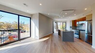 This contemporary single-floor space showcases a thoughtfully designed open-concept layout that seamlessly connects the living area and kitchen. Wide-plank light oak hardwood flooring runs throughout, lending warmth and continuity to the space. Oversized black-framed floor-to-ceiling windows and sliding glass doors flood the interior with abundant natural light while framing impressive city skyline views and lush outdoor greenery.

The kitchen is a standout feature, centered around a large island with a dark granite countertop and integrated sink. Warm wood cabinetry is complemented by white upper cabinets, a subway tile backsplash, and stainless steel appliances including a gas range and French door refrigerator. Recessed lighting and a tray ceiling detail above the kitchen add architectural interest.

The living area is generously proportioned and bright, with direct access to a private outdoor balcony through floor-to-ceiling sliding doors. A separate bedroom offers a serene retreat, also benefiting from large windows and natural light.

The bathroom is finished to a high standard, featuring floor-to-ceiling textured tile, a frameless sliding glass shower enclosure, mosaic tile flooring, and a sleek dark wood vanity with a granite countertop. Every detail reflects a commitment to modern, refined design.