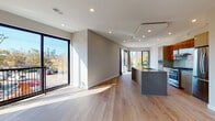 This contemporary single-floor space showcases a thoughtfully designed open-concept layout that seamlessly connects the living area and kitchen. Wide-plank light oak hardwood flooring runs throughout, lending warmth and continuity to the space. Oversized black-framed floor-to-ceiling windows and sliding glass doors flood the interior with abundant natural light while framing impressive city skyline views and lush outdoor greenery.

The kitchen is a standout feature, centered around a large island with a dark granite countertop and integrated sink. Warm wood cabinetry is complemented by white upper cabinets, a subway tile backsplash, and stainless steel appliances including a gas range and French door refrigerator. Recessed lighting and a tray ceiling detail above the kitchen add architectural interest.

The living area is generously proportioned and bright, with direct access to a private outdoor balcony through floor-to-ceiling sliding doors. A separate bedroom offers a serene retreat, also benefiting from large windows and natural light.

The bathroom is finished to a high standard, featuring floor-to-ceiling textured tile, a frameless sliding glass shower enclosure, mosaic tile flooring, and a sleek dark wood vanity with a granite countertop. Every detail reflects a commitment to modern, refined design.