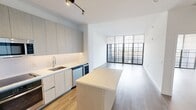 This modern 1-bedroom, 1-bathroom residence in Miramar, FL offers a thoughtfully designed open-concept layout with clean lines and contemporary finishes throughout. Light wood-tone flooring flows seamlessly across the entire space, complementing the crisp white walls and creating a bright, cohesive aesthetic.

The combined kitchen and living area serves as the heart of the home. The kitchen is outfitted with sleek, light wood-grain cabinetry extending to the ceiling for generous storage, quartz countertops, a large island, and a full suite of stainless steel appliances including a built-in oven, cooktop, microwave, dishwasher, and a wine cooler. The living area is anchored by striking floor-to-ceiling black-framed glass doors that open to a private balcony, flooding the space with natural light and offering open outdoor views.

The spacious primary bedroom features a ceiling fan, a large closet, and its own set of floor-to-ceiling glass doors leading to the balcony, continuing the airy, light-filled feel. The bathroom is finished in a clean, all-white palette with a soaking tub and shower combination, a wood-toned vanity, and warm wood flooring, delivering a spa-like atmosphere. This well-appointed residence combines modern design with functional living in a polished, move-in ready package.