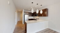 This single-floor residence presents a cohesive modern design throughout, combining clean lines, neutral tones, and quality finishes. The kitchen serves as a central highlight, featuring rich dark-brown cabinetry extending to the ceiling, stainless steel appliances including a range with an over-the-range microwave, and a white subway tile backsplash. A peninsula with a white countertop and an undermount sink provides additional workspace, while a series of decorative pendant lights hang overhead, contributing warmth to the contemporary aesthetic. Wood-look flooring runs through the main living and kitchen areas, connecting the space cohesively.

The hallway, finished in crisp white, leads to the bedrooms, which feature plush carpet flooring and generous closet space with built-in shelving systems. Large windows in the bedroom bring in natural light and offer views of the surrounding urban streetscape. Two bathrooms mirror each other in style, each appointed with marble-style tile flooring, a tub-shower combination, and a dark-wood vanity topped with white counters and a large mirror. A dedicated in-unit laundry closet houses a stacked washer and dryer, adding practical convenience to the overall layout.