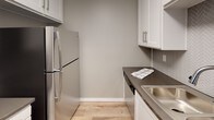 Located at 9128 Burke St in Pico Rivera, California, this single-story unit showcases a clean, contemporary aesthetic throughout. The open-concept layout connects the living area to the kitchen, creating a seamless flow ideal for everyday living and entertaining. Warm wood-tone laminate flooring runs through the main living spaces and bedrooms, while cool gray walls lend a modern, neutral palette across the entire unit.

The kitchen is thoughtfully appointed with crisp white cabinetry, dark countertops, a herringbone tile backsplash, stainless steel appliances including a refrigerator and microwave, and a peninsula with a built-in sink — offering both style and functionality. The adjacent living area is bright and open, with a wall-mounted air conditioning unit and access to a patio or balcony through vertical blinds.

The bedrooms feature the same warm flooring and neutral walls, each equipped with built-in sliding-door closets providing ample storage. The bathroom is finished with white subway tile surrounding a full bathtub and shower combo, complemented by chrome fixtures and clean, minimal detailing. Throughout, white baseboards and trim provide a polished contrast to the soft gray walls, giving the space a refreshed and move-in-ready feel.
