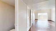 This two-story space is thoughtfully designed with distinct living areas spread across both levels. The main floor features rich hardwood flooring that extends through the open living area, where vaulted ceilings create a sense of height and volume. A large sliding glass door fitted with vertical blinds allows natural light to pour in while providing outdoor access. The staircase is neatly integrated into the living space, with a closet tucked beneath it for convenient storage.

The galley-style kitchen is well-appointed with white cabinetry, a mosaic tile backsplash, laminate countertops, and white appliances including a gas range and refrigerator. A double-basin sink sits beneath a window that brings in additional natural light, making the space feel open despite its efficient layout.

The upper level transitions to plush carpeting and features a generously sized open area, ideal for use as a loft or additional living space. Bedrooms on this level are carpeted and include closets, with at least one room offering sliding glass door access to an outdoor balcony with exterior views. The bathroom includes a full soaking tub, a vanity with storage, and textured walls throughout. Louvered closet doors and a textured ceiling are consistent details across the space.