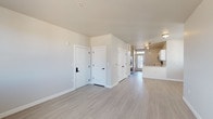 This two-story unit is designed with a clean, contemporary aesthetic and consistent finishes throughout both levels. Light wood-style luxury vinyl plank flooring runs continuously across the space, complementing the neutral gray-white wall tones and bright white trim and doors fitted with matte black hardware.

The kitchen is well-appointed with white shaker-style cabinetry extending to the upper walls, light quartz countertops with subtle veining, an undermount sink, and a full suite of stainless steel appliances including a range, over-the-range microwave, and dishwasher. A peninsula provides additional counter space and opens toward the adjacent living area. A door from the kitchen leads directly outside, adding convenient exterior access.

The main level also includes a half bathroom featuring a white vanity with an undermount sink and matching matte black fixtures. Multiple interior doors provide access to closets and utility areas along the main corridor.

The upper floor hosts generously sized rooms with large windows that allow ample natural light and exterior views. A full bathroom on this level includes a tub-shower combination, white vanity, and a window for natural light. An additional bathroom offers similar clean finishes. The staircase connecting both floors is open and well-integrated into the overall layout.