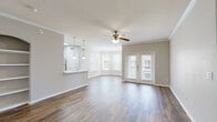 This single-floor residence offers a thoughtfully designed layout that balances comfort and functionality. The open-concept living and dining area serves as the heart of the home, showcasing rich hardwood flooring, crown molding, and a ceiling fan with integrated lighting. A bay window arrangement floods the space with natural light, while a set of French doors provides access to the outdoors. The kitchen is outfitted with white cabinetry, stainless steel appliances including a refrigerator, microwave, and range, complemented by a white quartz peninsula with an undermount sink and stylish pendant lighting overhead. A tile-floored entryway welcomes residents with convenient closet storage just inside the front door. The bedrooms are carpeted for warmth and comfort, each featuring a ceiling fan, natural light from windows with blinds, and closet access. The bathroom is finished with light tile flooring, gray cabinetry with ample drawer storage, a wide vanity with a white countertop, and a tiled tub and shower combination. Neutral tones throughout create a clean, cohesive aesthetic that suits a variety of interior styles.