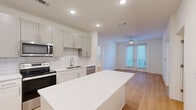 Located at 4939 Ohear Ave in North Charleston, SC, this two-bedroom, one-bathroom single-floor home offers a clean, modern design with a cohesive and functional layout. Light-toned wood-look flooring runs throughout the entire space, creating a warm, unified aesthetic.

The kitchen serves as a centerpiece, featuring gray shaker-style cabinetry, a white subway tile backsplash, a white quartz island, and a full suite of stainless steel appliances including a refrigerator, electric range, microwave, and dishwasher. Recessed lighting illuminates the space efficiently. The kitchen flows seamlessly into the living area, which is brightened by natural light streaming through French doors fitted with blinds and is equipped with a ceiling fan.

Both bedrooms are bright and simply designed with white walls, recessed lighting, and ample natural light from windows with blinds. The primary bedroom includes access to a walk-in closet with built-in shelving, adding practical storage. One bedroom features its own French doors, providing additional outdoor access and light.

The bathroom is well-appointed with a white vanity, quartz countertop, large framed mirror, and a tub-shower combination. The adjacent walk-in closet enhances the utility of this area. The overall design is clean and contemporary, making this an efficiently organized and inviting home.