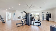 Located in the Bellalago community of Kissimmee, Florida, this Yardly fitness center offers a generously sized, single-floor exercise room designed to support a comprehensive workout routine. The space is finished with light hardwood-style flooring and crisp white walls, creating a clean, energizing atmosphere throughout.

The room is well-lit by a combination of recessed ceiling lights and large windows that invite abundant natural light while offering views of the surrounding community landscape. A large ceiling fan ensures steady air circulation, keeping the environment comfortable during workouts.

The facility is equipped with an impressive array of commercial-grade fitness equipment. Cardio options include multiple treadmills with interactive display screens, a stationary spin bike, a stair climber, and an elliptical trainer. Strength training is well-represented with a multi-station cable and resistance machine, a rowing machine, a squat rack, and a dumbbell rack stocked with a full range of free weights. A wall-mounted flat-screen television adds an entertainment element to the space.

A water fountain is conveniently installed along one wall, and a dedicated alcove area provides additional space for stretching or isolated exercises. The overall layout is thoughtfully organized to maximize usability, making this fitness center a well-rounded amenity for residents of the Bellalago community.