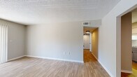 This single-floor space is designed with a clean, neutral aesthetic that creates a cohesive and functional living environment. The main living area features light hardwood-style flooring that extends throughout the entry and common spaces, complemented by soft gray walls and crisp white baseboards. A textured popcorn ceiling adds a subtle architectural detail overhead, while a large sliding door fitted with vertical blinds allows natural light to fill the room.

The kitchen is equipped with light gray cabinetry paired with white countertops and a beveled white subway tile backsplash. A double stainless steel sink with a matte black pull-down faucet serves as a practical focal point, and upper and lower cabinets provide ample storage.

Two bedrooms are finished with wall-to-wall carpet in a neutral tone, offering a comfortable and quiet atmosphere. Each room includes a window fitted with horizontal blinds, providing views of surrounding greenery and allowing natural light in. Closet access is available within the bedroom areas.

The bathrooms are functionally appointed, each featuring a full soaking tub and shower combination with built-in shelving, a toilet, and a brushed nickel towel bar, all finished in clean white tones.