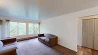 Located at 1424 E Grand River Ave in East Lansing, Michigan, this single-floor unit offers a straightforward and functional layout suited for everyday living. The living area is carpeted and bathed in natural light through a wide set of windows that frame lush, green tree views — creating a calm, nature-connected atmosphere. A wall-mounted AC unit provides climate control, and a baseboard heating system runs along the exterior walls throughout the unit.

The kitchen is efficiently designed with white cabinetry offering ample storage above and below the countertops, a single-basin sink, light wood-look vinyl flooring, and includes a coil-burner electric range and a full-size refrigerator.

The bedroom is generously sized, featuring plush carpeting and large windows that continue the unit's theme of abundant natural light and outdoor greenery. The clean white walls and neutral tones create a bright, open feel.

The bathroom includes a vanity with under-sink storage, a large mirror, a tub-shower combination, and rich wood-look flooring, providing a clean and practical space.

Overall, this unit presents a clean, no-frills interior with consistent design elements — neutral walls, carpet in living spaces, and an emphasis on natural light — making it a comfortable and practical residence near Michigan State University.