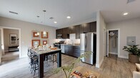 Located at Rampart Hills View in Colorado Springs, Colorado, this single-floor residence offers a thoughtfully designed layout with modern finishes and a cohesive aesthetic throughout. The kitchen is a standout feature, showcasing dark espresso cabinetry that reaches toward the ceiling, granite countertops, a classic white subway tile backsplash, and a full suite of stainless steel appliances including a range, microwave, dishwasher, and refrigerator. A granite-topped island with bar seating provides an ideal space for casual dining and entertaining. The living room is bright and inviting, with large windows dressed in neutral curtains that allow ample natural light to fill the space. Warm-toned accents complement the soft neutral palette, creating a welcoming ambiance. The bedroom offers a comfortable retreat, complete with a ceiling fan, a window with roller shade and drape treatments, and plush carpeting. The bathroom is elegantly finished with an extended dark-cabinetry vanity, dual sinks set in granite countertops, a large mirror, and wood-look flooring that ties seamlessly into the rest of the home. Throughout the residence, light wood-look flooring, recessed lighting, and clean white walls contribute to a polished, contemporary feel.