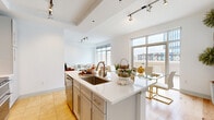 Located in the heart of Charlotte's vibrant South End neighborhood, this single-floor residence offers a thoughtfully designed open-concept layout that maximizes every square foot. The combined living and dining area is bathed in natural light from large floor-to-ceiling windows, which frame sweeping urban views and open to an outdoor terrace. Light hardwood flooring flows throughout the main living spaces, lending warmth to the clean, contemporary aesthetic defined by crisp white walls and track lighting.

The kitchen is a standout feature, anchored by a generous island with a white quartz countertop and undermount sink. Stainless steel appliances, including a double oven range and over-range microwave, are complemented by a herringbone tile backsplash and gray shaker cabinetry, creating a sleek, functional workspace that integrates seamlessly with the dining and living areas.

Both bathrooms are well-appointed, with the primary bath showcasing a long vanity with quartz countertops, framed mirrors, and warm travertine tile flooring that extends into the soaking tub surround. A spacious walk-in closet with built-in shelving provides ample storage. The hallway also accommodates a full-size washer and dryer with overhead cabinetry, adding exceptional convenience to this polished urban residence.
