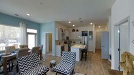 Located at 1817 Sir Tyler Dr in Wilmington, NC, this single-story home offers a well-designed open-concept floor plan that seamlessly connects the living, dining, and kitchen areas into one cohesive and inviting space. The kitchen is a standout feature, outfitted with white shaker-style cabinetry, a classic subway tile backsplash, stainless steel appliances including a refrigerator and range, and a central island with bar seating — ideal for both meal preparation and casual dining. Pendant lighting above the island adds a stylish focal point, while recessed ceiling lights ensure the entire space is well-illuminated. The light wood-style flooring runs throughout, complementing the soft blue-gray accent walls that give the home a relaxed coastal character consistent with its Wilmington setting. The living area flows naturally from the kitchen, providing ample room for seating and entertaining. Large windows allow natural light to filter in, enhancing the open and airy atmosphere of the home. Clean architectural lines, neutral tones, and thoughtful finishes come together to create a space that is both functional and aesthetically pleasing — a comfortable, move-in-ready home in a welcoming coastal community.