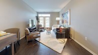 Located at 3450 E Walton Blvd in Auburn Hills, Michigan, this single-floor residence offers a thoughtfully designed open-concept layout that connects the kitchen, dining, and living areas into a cohesive, comfortable living environment. Rich dark hardwood flooring flows throughout the main living spaces, creating a warm and grounded aesthetic that contrasts elegantly with the neutral gray walls and white trim.

The kitchen is equipped with stainless steel appliances, including a full-size refrigerator, range, and microwave, complemented by white cabinetry, wood-accented lower cabinets, and granite countertops. A breakfast bar with seating extends from the kitchen island, making it ideal for casual dining. Track lighting overhead provides functional illumination throughout.

The living room receives generous natural light through multiple windows fitted with horizontal blinds, offering views of the surrounding greenery. The bedroom features plush carpeting, multiple windows, and a calm, neutral color palette that promotes a restful atmosphere. The primary bathroom includes a dual-sink vanity with white cabinetry, a walk-in shower, and dark hardwood flooring. A secondary bathroom features a full tub-shower combination. A dedicated laundry room houses a full-size washer and dryer alongside a water heater, adding everyday convenience.