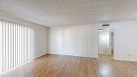 This 1-bedroom, 1-bathroom single-floor residence offers a thoughtfully arranged layout across a compact yet functional footprint. The living room is a bright, open space featuring warm wood-look laminate flooring, crisp white walls, and a textured ceiling. A large sliding glass door fitted with vertical blinds allows natural light to fill the room, creating an airy atmosphere. A small pass-through window connects the living area to the kitchen, adding a practical touch to the open feel of the space.

The bedroom is a comfortable, well-sized room with soft carpeting underfoot, neutral walls, and a textured ceiling. A window with blinds provides natural light and outside views. The bedroom connects directly to a walk-in closet, which features multiple hanging rods on three walls and a freestanding shelving unit, offering generous storage and organization options.

The bathroom is clean and functional, featuring wood-look flooring, a dark-finished vanity topped with a granite-style countertop, a framed mirror, and a full tub-shower combination with white tile surround. The layout is efficient and well-appointed. Throughout the residence, the consistent use of light tones and neutral finishes creates a cohesive, move-in-ready environment suited for comfortable everyday living.