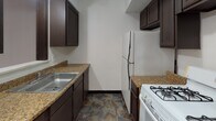 Located at 2109 Collingwood Blvd in Toledo, Ohio, this single-floor unit offers a straightforward and functional layout connecting several distinct living areas. Warm hardwood flooring runs throughout the main living spaces and rooms, providing a consistent and classic aesthetic across the unit.

The living area is open and simply appointed, featuring white walls, dark baseboards, and a pass-through window that connects directly to the kitchen, adding a sense of openness between the two spaces. A hallway extends from the main living area, leading to additional rooms and providing clear circulation throughout the unit.

The bedrooms are well-proportioned, each featuring the same hardwood flooring and white walls. Windows fitted with horizontal blinds allow natural light to filter in, offering views of the surrounding neighborhood. Baseboard heating units are present in these rooms, providing a practical heating solution.

The kitchen is efficiently designed with dark espresso cabinetry, granite-toned countertops, a double-basin stainless steel sink, a gas range, and a full-size refrigerator. Stone-patterned tile flooring grounds the space and distinguishes it from the hardwood in adjacent areas.

The bathroom continues the stone-patterned tile flooring and includes a vanity with sink, a standard toilet, and a tiled tub-shower combination, completing the unit's functional amenities.