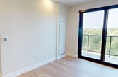 This contemporary 530-square-foot, one-bedroom, one-bathroom unit at 2310 Richmond Street in London, Ontario offers a thoughtfully designed single-floor layout with modern finishes throughout. Light hardwood flooring runs continuously across the open living areas, complementing the clean white walls and recessed pot lighting that create a bright, airy atmosphere.

The living area features a sleek sliding glass door leading to a private balcony, offering elevated treetop views of lush greenery — a standout feature of the unit. The kitchen is equipped with warm wood cabinetry, white upper cabinets, stainless steel appliances, and a functional island, making efficient use of the available space.

The bedroom, spanning 100 square feet, is highlighted by large floor-to-ceiling windows framed in black that flood the room with natural light and provide panoramic outdoor views. A bold blue accent wall adds a striking design element to this private retreat.

The bathroom is appointed with elegant deep-blue glazed subway tile surrounding a soaker tub and shower combination, paired with matte black fixtures for a sophisticated, contemporary finish.

A hallway connects the spaces efficiently, with a mirrored sliding-door closet adding functionality. This unit combines modern urban design with natural surroundings for a refined living experience.