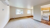 Located at 8415 NE Hazel Dell Ave in Vancouver, WA, this one-bedroom, one-bathroom unit offers a practical and well-designed single-floor layout. The combined kitchen and living area serves as the heart of the unit, with the living space featuring neutral carpet flooring, warm wood baseboards, and two windows that invite natural light and outdoor views. A wall-mounted mini-split unit provides efficient climate control. The kitchen is functional and well-appointed, featuring warm wood cabinetry, a full-size refrigerator, a sink with ample counter space, and a convenient built-in breakfast bar with seating. Hardwood-style flooring ties the kitchen together with a clean, easy-to-maintain aesthetic. The bedroom is a comfortable, carpeted retreat with a window providing natural light, and it connects conveniently to a dedicated closet. The full bathroom includes a tub/shower combo, a vanity with warm wood cabinetry, and tile-style flooring, maintaining the unit's cohesive neutral palette throughout. Neutral warm-white walls are consistent across all rooms, creating a bright and unified ambiance that makes the space feel open and welcoming throughout.