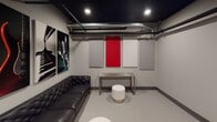 This single-floor recording studio lounge is thoughtfully designed for both function and atmosphere. The space features a striking dark ceiling with exposed ductwork and beam detailing, creating an industrial yet polished aesthetic that sets the tone throughout. The walls are finished in a neutral gray and lined with acoustic treatment panels — a combination of white and bold red fabric panels — strategically placed to optimize sound control and minimize unwanted reflections. A tufted black leather sofa anchors the seating area, complemented by round white ottomans and a minimalist metal console table, offering a comfortable yet professional environment. Music-themed artwork, including large-format prints of a guitar, piano keys, and a vintage microphone, adds character and reinforces the creative purpose of the space. The entry features a heavy-duty door with a hydraulic closer and a stainless steel kick plate, ensuring acoustic isolation. Recessed lighting provides even, functional illumination throughout. The light gray flooring contrasts cleanly with the dark ceiling, contributing to a balanced, studio-quality interior. Overall, this space is well-suited as a green room, listening lounge, or client waiting area within a professional audio recording facility.