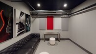 This single-floor recording studio lounge is thoughtfully designed for both function and atmosphere. The space features a striking dark ceiling with exposed ductwork and beam detailing, creating an industrial yet polished aesthetic that sets the tone throughout. The walls are finished in a neutral gray and lined with acoustic treatment panels — a combination of white and bold red fabric panels — strategically placed to optimize sound control and minimize unwanted reflections. A tufted black leather sofa anchors the seating area, complemented by round white ottomans and a minimalist metal console table, offering a comfortable yet professional environment. Music-themed artwork, including large-format prints of a guitar, piano keys, and a vintage microphone, adds character and reinforces the creative purpose of the space. The entry features a heavy-duty door with a hydraulic closer and a stainless steel kick plate, ensuring acoustic isolation. Recessed lighting provides even, functional illumination throughout. The light gray flooring contrasts cleanly with the dark ceiling, contributing to a balanced, studio-quality interior. Overall, this space is well-suited as a green room, listening lounge, or client waiting area within a professional audio recording facility.