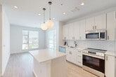 This thoughtfully designed 2-bedroom, 3-bathroom residence at 6402 America Blvd in Hyattsville, MD offers a clean, contemporary aesthetic across its single floor. The entrance opens into a bright hallway with light wood-style flooring that flows seamlessly throughout the space, setting a warm and modern tone.

The open-concept kitchen and living area serves as the heart of the home. The kitchen is outfitted with crisp white cabinetry, a herringbone-patterned tile backsplash, stainless steel appliances including a range, microwave, and dishwasher, and a sleek white island with pendant globe lighting overhead. Large windows flood the adjacent living area with natural light and provide views of the surrounding neighborhood.

The spacious primary bedroom offers generous proportions, double-door closet storage, and natural light from a large window. The second bedroom is equally well-lit, featuring its own window and access to a nearby bathroom. Seven closets throughout the unit provide exceptional storage options.

All three bathrooms showcase elegant marble-look tile flooring, white subway tile surrounds, and white vanities with matte black hardware accents. One bathroom features a glass-enclosed walk-in shower, while another includes a full soaking tub. The overall design is cohesive, bright, and modern, creating a polished living environment.
