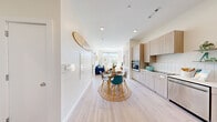 This well-designed single-floor residence offers a thoughtful open-concept layout that seamlessly connects the kitchen, dining, and living areas. Light wood-tone cabinetry lines the galley-style kitchen, which is equipped with stainless steel appliances including a French door refrigerator with ice maker, dishwasher, built-in oven, and a cooktop — all complemented by clean white countertops and a classic subway tile backsplash. The dining area comfortably accommodates a round table, flowing naturally into the sun-drenched living room, where expansive windows frame outdoor views and fill the space with abundant natural light. Light-toned hardwood-style flooring runs throughout the main living areas, enhancing the bright, airy atmosphere. The bedroom is a calm retreat with plush carpeting, large dual windows offering urban views, and a dedicated walk-in closet with wire shelving for organized storage. The full bathroom features large-format tile flooring, a walk-in shower with vertical subway tile surround, and a floating vanity with an integrated sink. The overall aesthetic is clean and contemporary, with a cohesive neutral palette that makes the space feel open and inviting throughout.