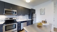 Located at 6300 City Avenue in Philadelphia, PA, this single-floor residence offers a thoughtfully designed living space with modern finishes throughout. The kitchen is a standout feature, showcasing sleek dark cabinetry with brushed hardware, bright white quartz countertops, and a classic subway tile backsplash that adds texture and depth. Stainless steel appliances — including a range, microwave, dishwasher, and refrigerator — provide both functionality and a polished aesthetic. A large kitchen island or peninsula extends the counter space, making it ideal for meal preparation and casual dining. The light wood-style flooring runs throughout, contributing to a warm yet contemporary atmosphere. Neutral wall tones and flush ceiling lighting keep the space bright and airy. The open-concept design allows for a seamless flow between the kitchen and living areas, maximizing the sense of space. The overall ambiance is clean, modern, and move-in ready, with carefully selected finishes that reflect a high standard of contemporary residential design. This unit is well-suited for those seeking a stylish, functional home in the City Avenue corridor of Philadelphia.