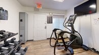 Located at 710 Yorkmont Rd in Charlotte, NC, this fitness center is a efficiently organized exercise space designed to support a well-rounded workout routine. The room features durable wood-look flooring throughout, white walls, and a textured ceiling fitted with track lighting that provides consistent, bright illumination across the workout area.

The exercise room is equipped with key cardio machines, including a treadmill and an elliptical trainer, positioned to allow comfortable use. A large wall-mounted flat-screen television faces the equipment, offering entertainment during workouts. A full-length mirror on one wall enhances the sense of space and allows users to monitor their form. A rack of free weights is also visible, adding strength-training options to the facility.

A bank of gray metal lockers lines one wall, providing secure personal storage for users. A posted fitness center rules board and workout guide are mounted near the entrance, keeping users informed. The space also benefits from direct access to an ADA-compliant restroom, conveniently located just outside the exercise room. Safety features include clearly marked exit signage and an emergency alarm panel. The layout is practical and straightforward, making this fitness center a functional amenity for everyday use.