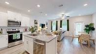 This two-story home is thoughtfully designed across two levels, offering a functional and comfortable layout with 3 bedrooms and 3 bathrooms. The main floor features an open-concept living area where the kitchen, dining room, and living room flow seamlessly together. The kitchen is outfitted with white shaker-style cabinetry, granite countertops, stainless steel appliances including a dishwasher, electric range, and built-in microwave, and a central island with a sink. Light wood-style flooring runs throughout the main level, complementing the bright, neutral color palette. The living room is illuminated by natural light from multiple windows dressed with green curtains, and a ceiling fan adds to the comfort of the space. The dining area provides a dedicated space for meals adjacent to the kitchen. Upstairs, the primary bedroom is generously sized and includes a spacious walk-in closet with wire shelving. The additional bedrooms each feature closets with double-panel doors and carpeted flooring. The bathrooms are finished with white vanities and granite countertops, consistent with the home's cohesive design language. A dedicated laundry room houses a full-size washer and dryer with overhead wire shelving for added storage.