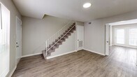 This two-story home in Macon, Georgia offers a practical and well-organized layout across two floors. The main level features wood-look vinyl flooring throughout, a carpeted staircase with a white metal railing, and an open living area that connects to the kitchen. The kitchen is equipped with warm wood cabinetry, stone-look countertops, black appliances including an electric range, and a built-in dishwasher, providing ample functionality for everyday cooking. The main level also includes access to the electrical panel and washer/dryer hookups, adding convenience for residents. Upstairs, two carpeted bedrooms offer comfortable retreats finished in neutral tones. The spacious primary bedroom includes a double-door closet and an additional separate closet, while the second bedroom features a window that brings in natural light. Both bathrooms are clean and functional — one includes a full tub/shower combo, while the other features a vanity with a white sink, a large wall mirror with modern lighting, and wood-look flooring. A hallway connects the upper-level rooms for easy accessibility. Throughout the home, neutral gray walls and white trim create a cohesive, move-in-ready aesthetic.