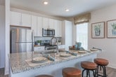 Located at 4251 Holly Springs Pkwy in Holly Springs, Georgia, this single-floor residence combines modern design with comfortable, functional living. The open-concept layout flows seamlessly from room to room, with wood-look flooring running through the main living areas and plush carpet in the bedrooms.

The kitchen is a standout feature, boasting tall white shaker cabinets, granite countertops, a subway tile backsplash, a large center island with a undermount sink, and a full suite of stainless steel appliances. Natural light fills the space through multiple windows dressed with wood blinds and sheer curtains.

The bright dining area is framed by a bay of windows on multiple walls, creating an airy, sunlit atmosphere ideal for gatherings. The living room offers a welcoming ambiance with a ceiling fan, large windows, and thoughtful design details.

The primary bedroom features a soft color palette with paneled wall accents, generous natural light, and plush carpet, offering a serene retreat. The secondary bedroom is equally well-sized and comfortable. The bathroom is finished with granite countertops, white cabinetry, wood-look flooring, and a tub-shower combination with white tile surround. Clean white five-panel interior doors complete the polished aesthetic throughout this thoughtfully designed home.