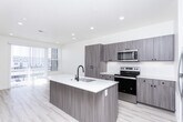Located in American Fork, Utah, this well-appointed 1-bedroom, 2-bathroom unit offers a thoughtfully designed single-floor layout that maximizes every square foot. The open-concept kitchen serves as the centerpiece of the living area, showcasing taupe flat-front cabinetry with matte black hardware, bright white quartz countertops, and a full suite of stainless steel appliances including a French door refrigerator, electric range, and built-in microwave. A large central island with an undermount sink and matte black faucet provides both additional prep space and a natural gathering point. Light hardwood-style flooring flows throughout the kitchen and common areas, complementing the clean, neutral palette. Recessed lighting and sliding glass doors with vertical blinds allow for ample natural light. The spacious primary bedroom features plush carpeting, a ceiling fan, generous windows with blinds, and direct access to a closet and full bathroom. The primary bath is finished with a single-sink vanity, white quartz countertop, and a tub/shower combo. A second full bathroom mirrors the same clean, modern finishes. The overall aesthetic is contemporary and light-filled, with a cohesive design language throughout.