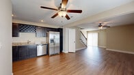 This two-story home offers a thoughtfully designed layout across two floors, providing ample space for comfortable living. The main floor features an open-concept kitchen and living area unified by warm hardwood-style flooring and ceiling fans throughout. The kitchen is well-appointed with dark cabinetry, granite countertops, stainless steel appliances including a French door refrigerator, dishwasher, range, and built-in microwave, plus a distinctive wine rack. The open living area is bright and spacious, with large windows allowing natural light to flow freely, and a staircase with classic balustrade leads to the upper floor. The upper level houses all four bedrooms, including a generously sized primary bedroom, along with three full bathrooms. The bedrooms feature plush carpeting, ceiling fans, and windows with pleasant outdoor views. The bathrooms are finished with dark vanity cabinetry, white fixtures, and hardwood-style flooring. Additional highlights include two closets, a hallway, and in-unit laundry access. The home's neutral color palette and clean finishes create a welcoming and functional living environment throughout.