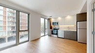 This thoughtfully designed single-floor unit offers a contemporary living experience with clean lines, modern finishes, and an efficient layout across four distinct areas. Light wood-tone flooring runs throughout, creating a warm and cohesive aesthetic that ties every room together.

The open-concept living and kitchen area is the heart of the space, bathed in natural light from expansive floor-to-ceiling windows and a sliding glass door that frame views of the surrounding urban streetscape. The kitchen is outfitted with two-tone cabinetry — combining white upper cabinets with warm wood-grain lower cabinets — complemented by a subtle herringbone tile backsplash, stainless steel appliances including a range, microwave, and dishwasher, and an undermount sink.

The bedroom is a bright, serene retreat featuring its own large floor-to-ceiling window with views of the neighboring brick building and tree canopy. A dedicated walk-in closet with built-in adjustable shelving provides generous, well-organized storage.

The bathroom is finished with large-format neutral floor tiles, full-height square subway wall tiles in the tub surround, a built-in shower niche, and chrome fixtures, offering a clean and functional design. White walls throughout the unit enhance the sense of openness and light, contributing to an overall ambiance that is modern, airy, and move-in ready.