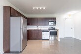 Located at 4981 Bathurst St in North York, Toronto, this 2-bedroom, 1-bathroom unit offers a well-organized single-floor layout with a functional and efficient use of space. The open-concept living and kitchen area anchors the unit, featuring a seamless transition between the parquet-floored living space and the tiled kitchen zone. The kitchen is fitted with rich dark-brown cabinetry, a white subway tile backsplash, light countertops, and a full suite of stainless steel appliances including a refrigerator, electric range, and over-the-range microwave. A large window in the living area fills the space with natural light and offers views of the surrounding Toronto cityscape. Both bedrooms feature classic parquet flooring and individual baseboard heating units, with windows overlooking urban rooftop and skyline views. The primary bedroom includes a mirrored sliding closet door, adding a sense of depth. The bathroom is finished with neutral-toned wall tiles, a combined soaker tub and shower with chrome fixtures, and a clean white vanity. Crisp white walls and consistent trim throughout the unit create a cohesive, clean aesthetic. The layout is complemented by a dedicated entry area with its own window and door access.