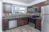 Located in Bloomfield Hills, Michigan, this single-floor residence offers a well-designed layout with a thoughtful blend of modern finishes and comfortable living spaces. The kitchen is a standout feature, showcasing rich dark espresso cabinetry, granite-style countertops, and a striking mosaic tile backsplash with warm tones of gold, brown, and charcoal. A full suite of stainless steel appliances — including a refrigerator, electric range, over-the-range microwave, and dishwasher — provides both functionality and a polished aesthetic. Wood-look flooring and a pendant light fixture above the sink add warmth and style, while a large window with vertical blinds fills the kitchen with natural light. The living areas are generously sized, featuring neutral-toned carpeting and multiple windows dressed in vertical blinds that allow abundant natural light throughout. The open layout creates a bright, airy atmosphere well-suited for both everyday living and entertaining. The bedrooms continue the carpeted, light-filled theme, each offering comfortable proportions and windows that bring in natural light. The bathroom features a full soaking tub with a clean white tile surround accented by a decorative mosaic border, providing a classic and functional design.