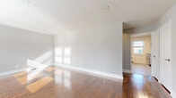 This single-floor unit showcases a thoughtfully arranged layout with rich, polished hardwood floors that run throughout the main living areas and bedrooms, lending warmth and character to the space. The open living area is generously proportioned, bathed in natural light from multiple windows, and features neutral gray walls, clean white baseboards, and recessed lighting. A wall-unit air conditioner and baseboard radiator provide year-round climate control, while the front entry door offers direct outdoor access with views of surrounding greenery.

The kitchen is efficiently designed with dark cabinetry, a classic subway tile backsplash, white countertops, and a full suite of stainless steel appliances including an electric range, built-in microwave, and dishwasher. Light-toned flooring in the kitchen provides a clean contrast to the rest of the unit.

The bedrooms are well-sized, each equipped with ceiling fans and hardwood floors. The primary bedroom includes two closets for ample storage. Additional bedrooms feature radiator heating and windows with natural light.

The bathroom is finished in crisp white tile, offering a clean, modern aesthetic with a mirrored vanity, a soaking tub with shower, and a window for ventilation. Overall, the space presents a bright, well-maintained environment with functional updates throughout.