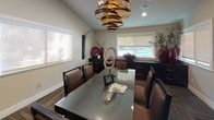 This single-story business center is thoughtfully designed to support professional needs in a polished, contemporary setting. The space is organized into distinct functional zones, beginning with a welcoming entry area that features hardwood flooring, large windows allowing ample natural light, and glass-paneled doors that create an open, transparent feel between areas.

The main conference area serves as a central focal point, anchored by a sleek glass-topped table surrounded by upholstered chairs. Vaulted ceilings add a sense of openness, while multiple windows fitted with roller shades provide controlled natural light. A dramatic spiral metallic chandelier overhead adds a striking design element, complementing the warm neutral wall tones and patterned carpet flooring.

Adjacent to the conference area is a dedicated workstation zone, equipped with built-in dark cabinetry, open shelving, granite-topped counters, and multiple computer stations. Recessed lighting illuminates the workspace effectively, and a glass-paneled door separates this area for privacy when needed.

Dark cabinetry, rich wood tones, and coordinated decor elements unify the space with a cohesive, modern aesthetic, making this business center both functional and professionally inviting.