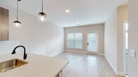 This single-floor unit presents a clean, contemporary design throughout its well-organized layout. The open-concept kitchen serves as a central feature, equipped with stainless steel appliances including a refrigerator, electric range, and over-the-range microwave. Warm wood-tone flat-panel cabinetry extends from floor to ceiling, complemented by white quartz countertops, a white subway tile backsplash, and matte black hardware. A peninsula with an integrated sink and pendant globe lighting above creates a natural transition into the adjacent living and dining area.

The living and dining space features light wood-look flooring, neutral beige walls, and access to a exterior door flanked by windows fitted with blinds, allowing ample natural light. The bedrooms are finished with plush neutral carpet and include ceiling fans and multi-pane windows that invite additional daylight. One bedroom offers notable wall height, enhancing the sense of openness.

The bathroom is outfitted with a tub-shower combination featuring white tile surround, matte black fixtures, a wood-tone vanity with a white countertop, and light wood-look flooring, maintaining the unit's cohesive modern aesthetic throughout.