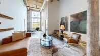 Located at 4147 E Main Street Ext in Spartanburg, SC, this thoughtfully converted loft blends historic industrial character with modern finishes. The open-plan kitchen and living area anchors the space, showcasing soaring ceilings with exposed wooden beams, polished concrete floors, and industrial-style ductwork that pays homage to the building's original architecture. The kitchen is well-appointed with stainless steel appliances, gray cabinetry, a white subway tile backsplash, granite countertops, and a central island with bar seating — ideal for both cooking and casual dining. A sliding barn door and original timber columns add distinctive architectural detail throughout. The living area benefits from an abundance of natural light pouring through large, arched industrial-style windows that frame views of the surrounding greenery, complemented by exposed original brick walls. The spacious primary bedroom continues the loft's aesthetic with soaring ceilings and oversized windows. Two bathrooms provide functional comfort, each finished with clean, modern fixtures. A dedicated laundry room with a full-size washer and dryer adds everyday convenience. The overall ambiance strikes a refined balance between raw, historic character and contemporary residential comfort.