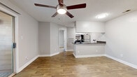 Located at 1700 Chambers Dr in Matthews, NC, this single-floor unit offers a well-designed, functional layout with a clean, modern aesthetic throughout. The open-concept living area features warm wood-look flooring, neutral gray walls, and a ceiling fan with integrated lighting, creating a bright and comfortable atmosphere. A peninsula-style kitchen serves as the centerpiece, equipped with dark granite-style countertops, white cabinetry, stainless steel appliances including a refrigerator and range, and a double-basin sink — all oriented to face the living area for a connected, social feel. Additional galley-style kitchen storage provides ample cabinetry and counter space. The living area includes a sliding glass door that opens to a private deck, offering outdoor views of surrounding trees and greenery, and inviting natural light into the interior. The bedrooms are carpeted for comfort and each include ceiling fans. At least one bedroom features a walk-in closet and direct access to a bathroom with vanity. A dedicated entryway with a coat closet provides a practical transition into the main living space. Overall, the unit presents a tidy, move-in-ready environment with consistent finishes and thoughtful design details throughout.