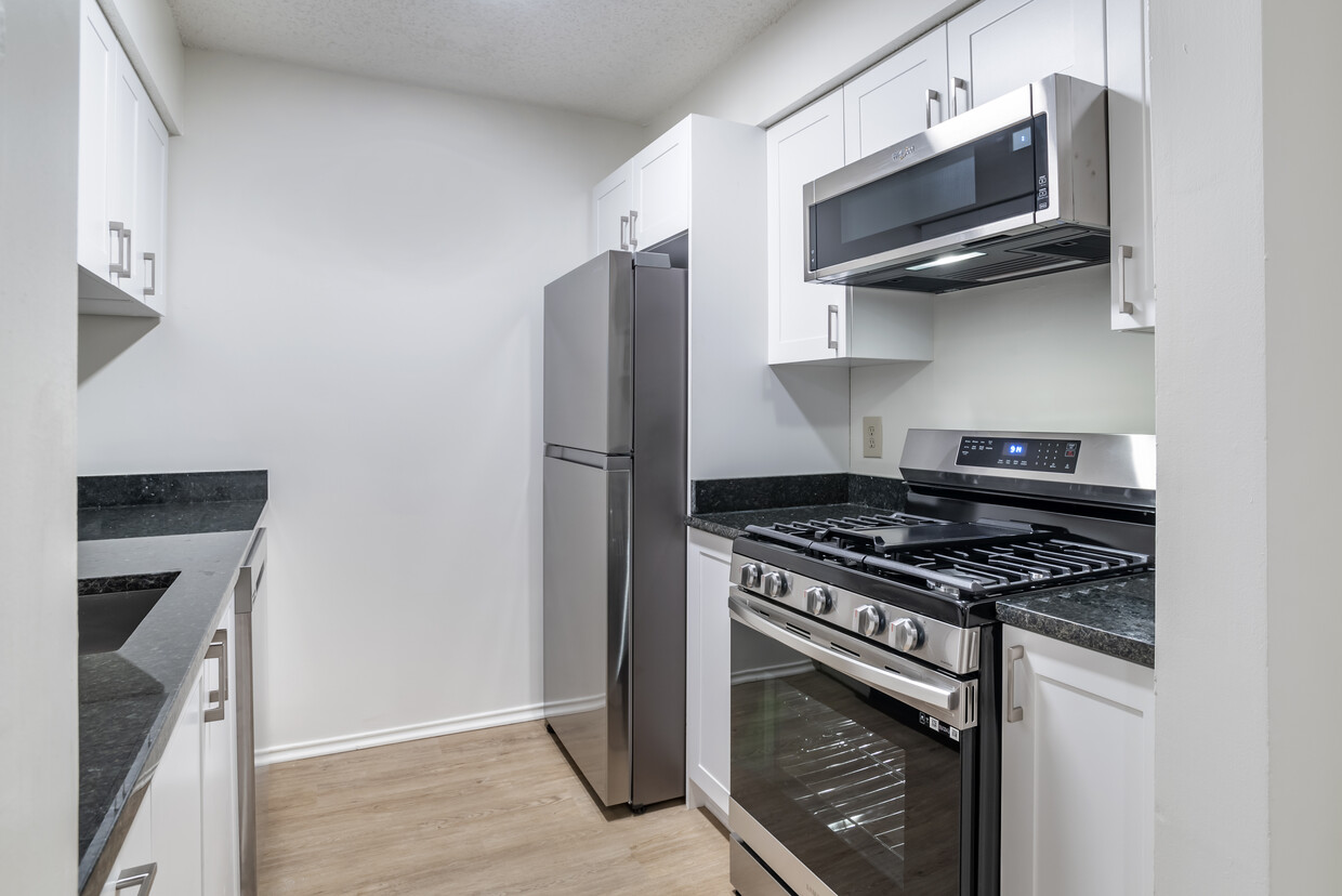 Renovated Package II kitchen with stainless steel appliances, granite countertops, white cabinetry, and hard surface flooring - eaves Fair Lakes